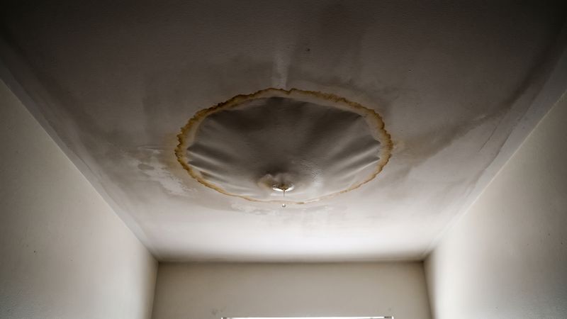 Amber-ringed AC leak water stain on a ceiling, the drywall sagging into a bulge with a drop forming