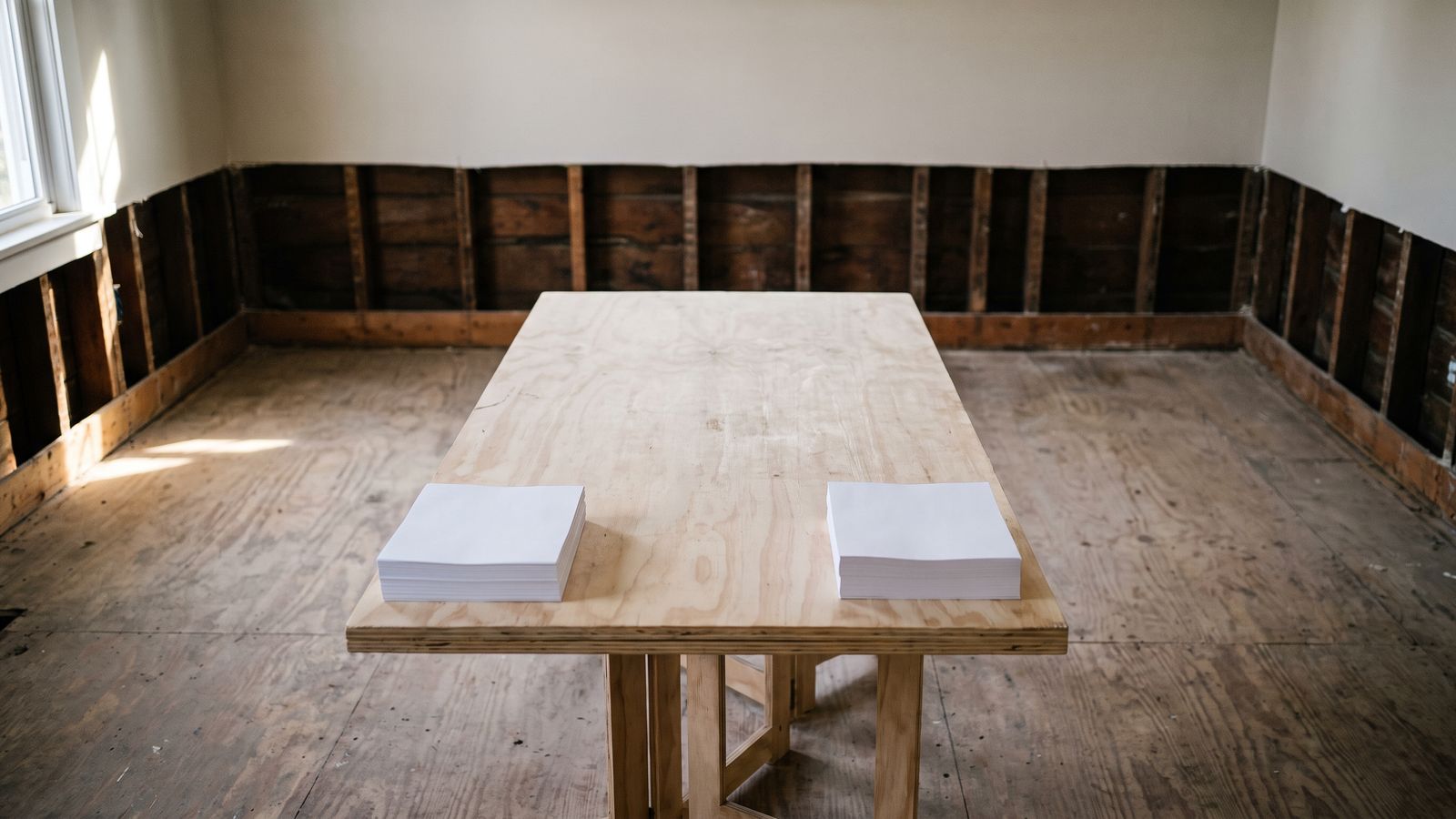 Two paper stacks on a table Two squared stacks of blank paper sitting apart on a plywood table in a stripped wood-framed room.