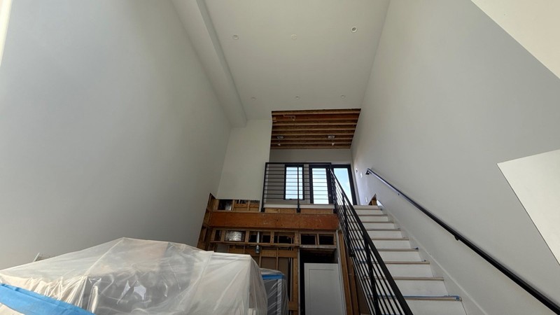A tall stairwell with the ceiling drywall removed to the joists and a wall opened down to bare studs