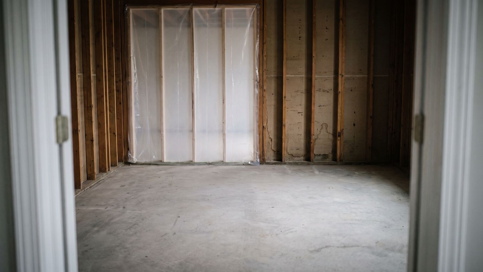 Stripped framing behind taped containment sheeting Bare studs and a swept slab behind taped poly sheeting after moldy drywall removal, the answer to black mold vs regular mold