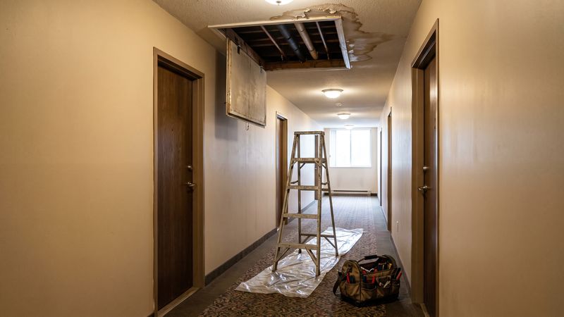 Ceiling access panel hinged open below a corridor water stain, where a condo master policy deductible question starts.