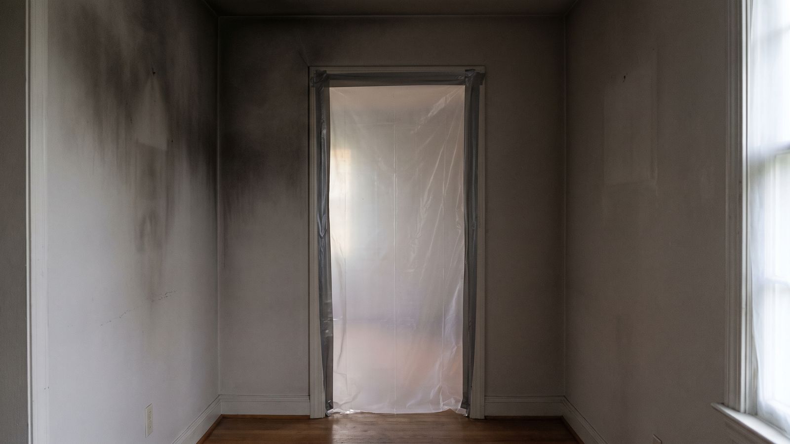 Plastic sheeting taped over a doorway beside a soot-stained wall during fire and smoke damage restoration