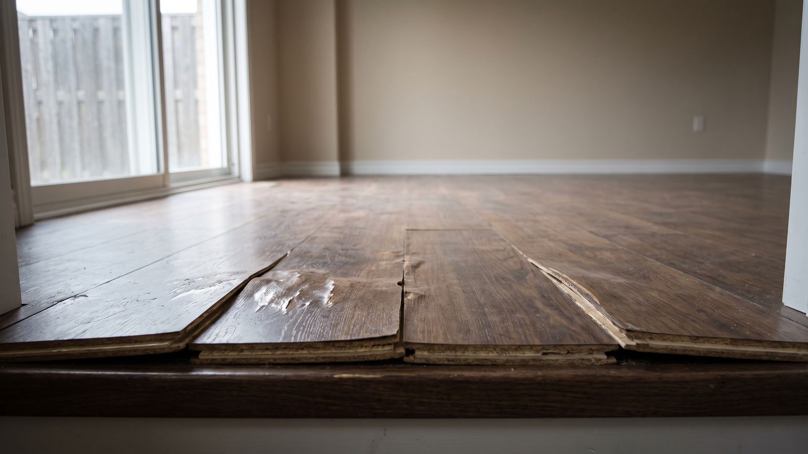 Engineered plank flooring at a threshold, veneer peeled back from the layered core, hardwood floor water damage
