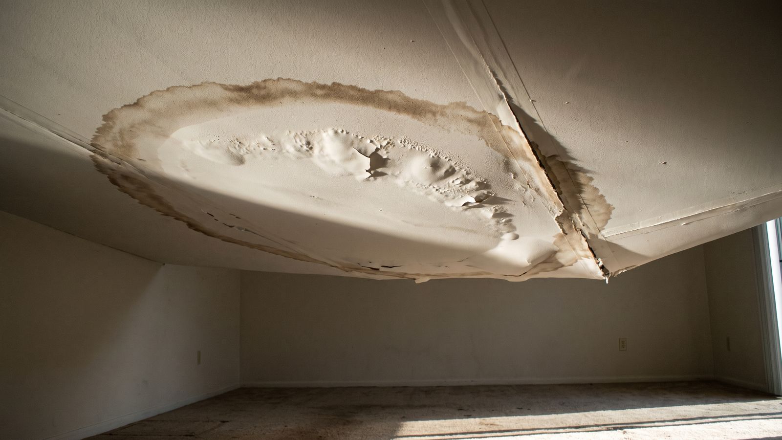 Sagging drywall ceiling under a wide brown water stain, an early sign of water damage