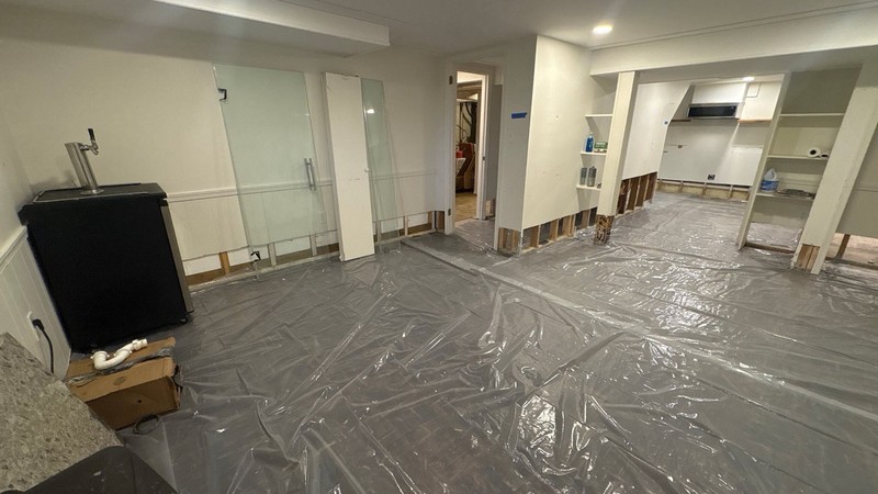 Basement walls cut open above the baseboard to bare studs, with plastic sheeting laid across the floor