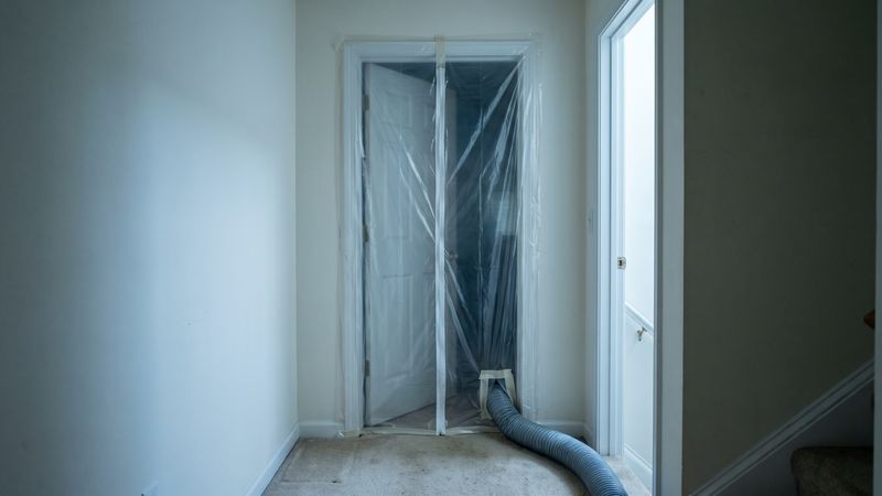 Basement doorway sealed floor to ceiling with mold containment sheeting, exhaust duct run out through a taped sleeve.