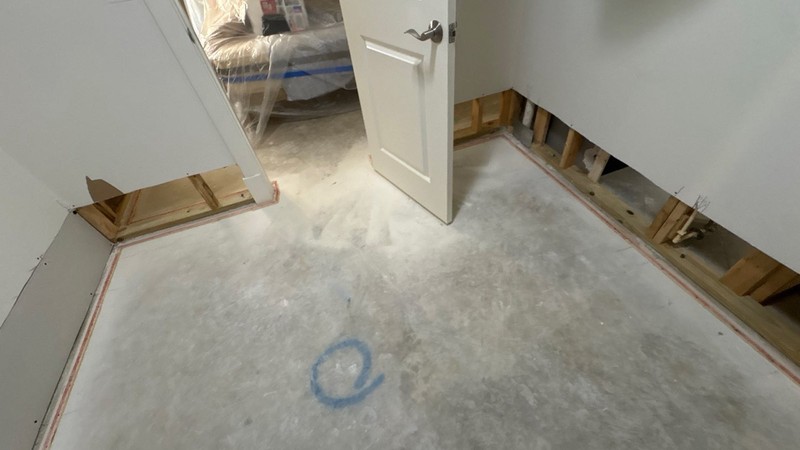 A room stripped down to its concrete slab, the lower drywall cut away to expose the wall studs