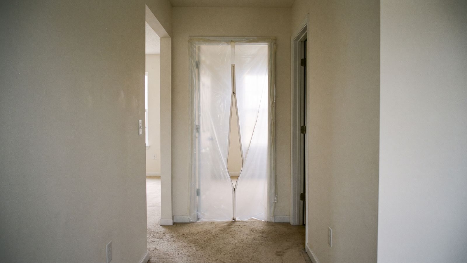 Plastic sheeting containment at a doorway Doorway sealed with clear plastic sheeting and a zippered entry for mold containment before a wall is opened.