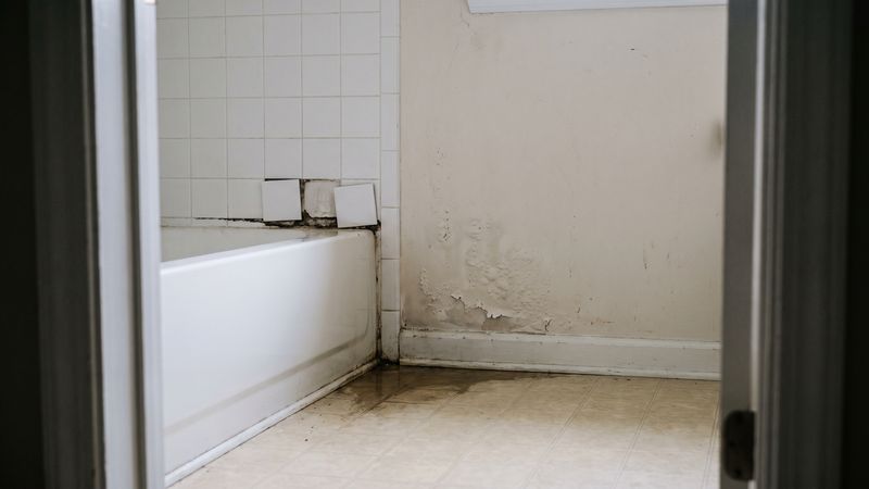 Loose shower wall tiles, a blackened tub seam and blistered paint show classic pipe leak behind shower wall signs