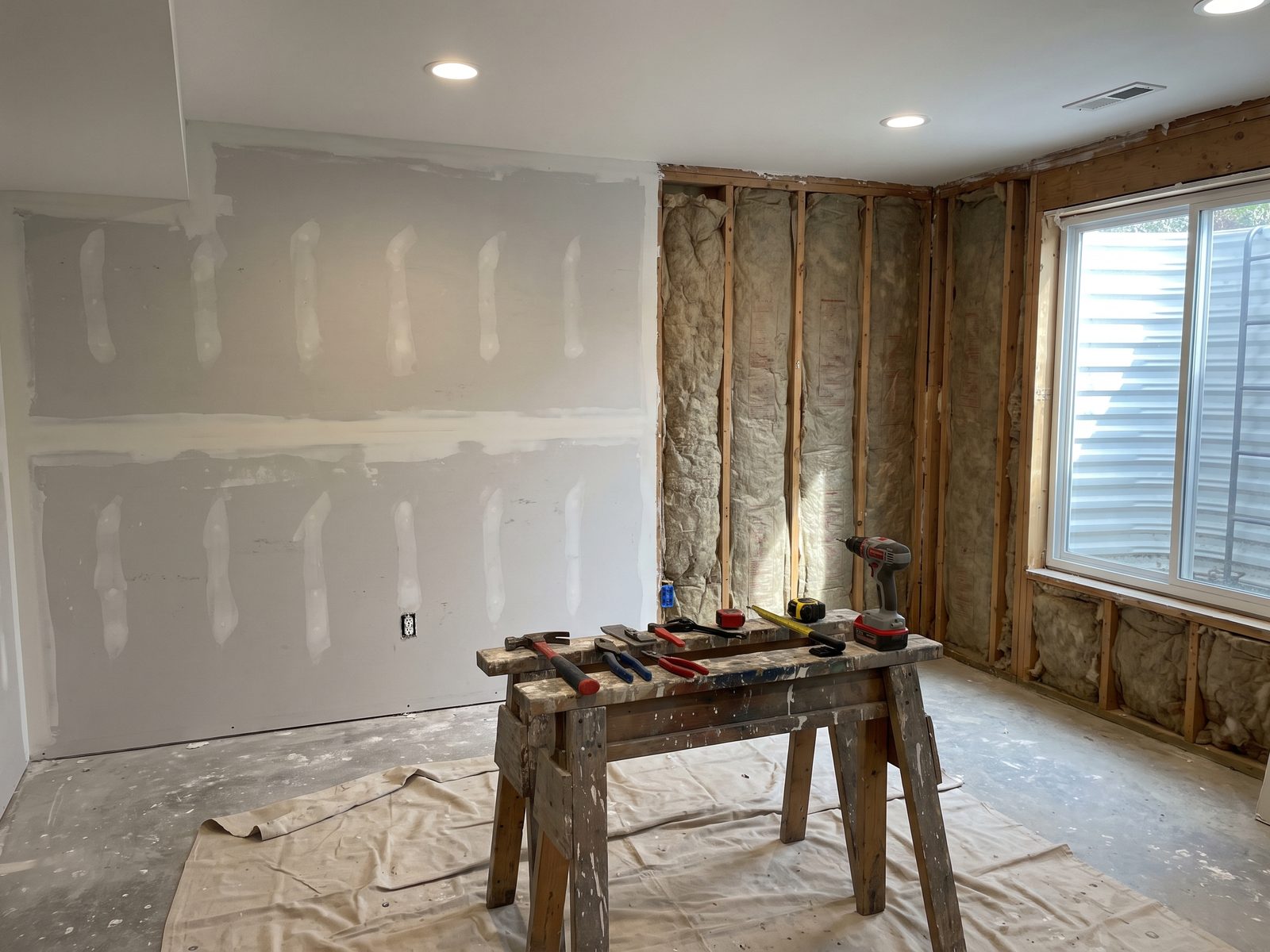 Basement mid-rebuild with new drywall hung and taped on one wall and the adjoining wall still open to studs.