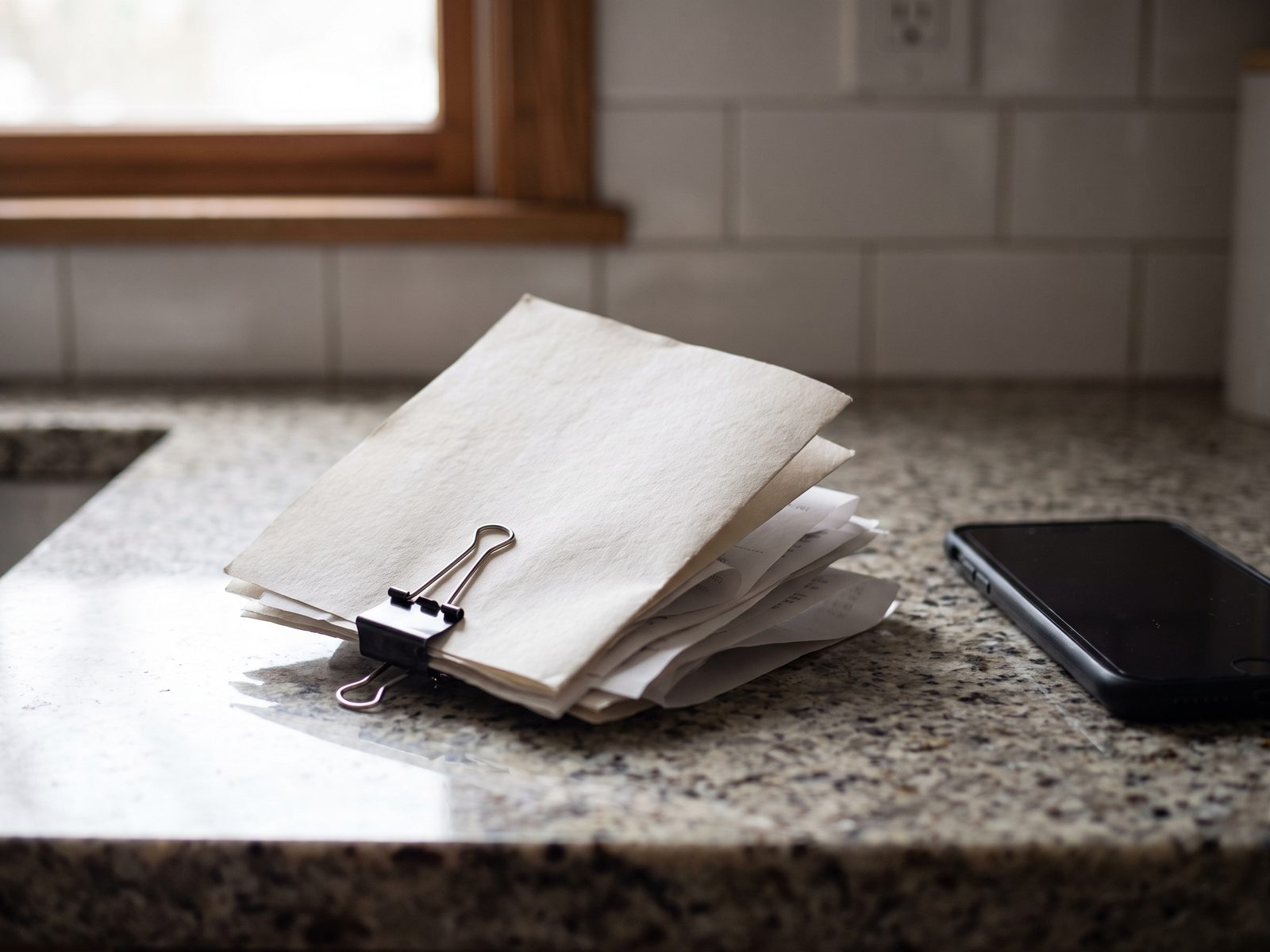 Small clipped stack of completion paperwork and receipts on a kitchen counter beside a phone.