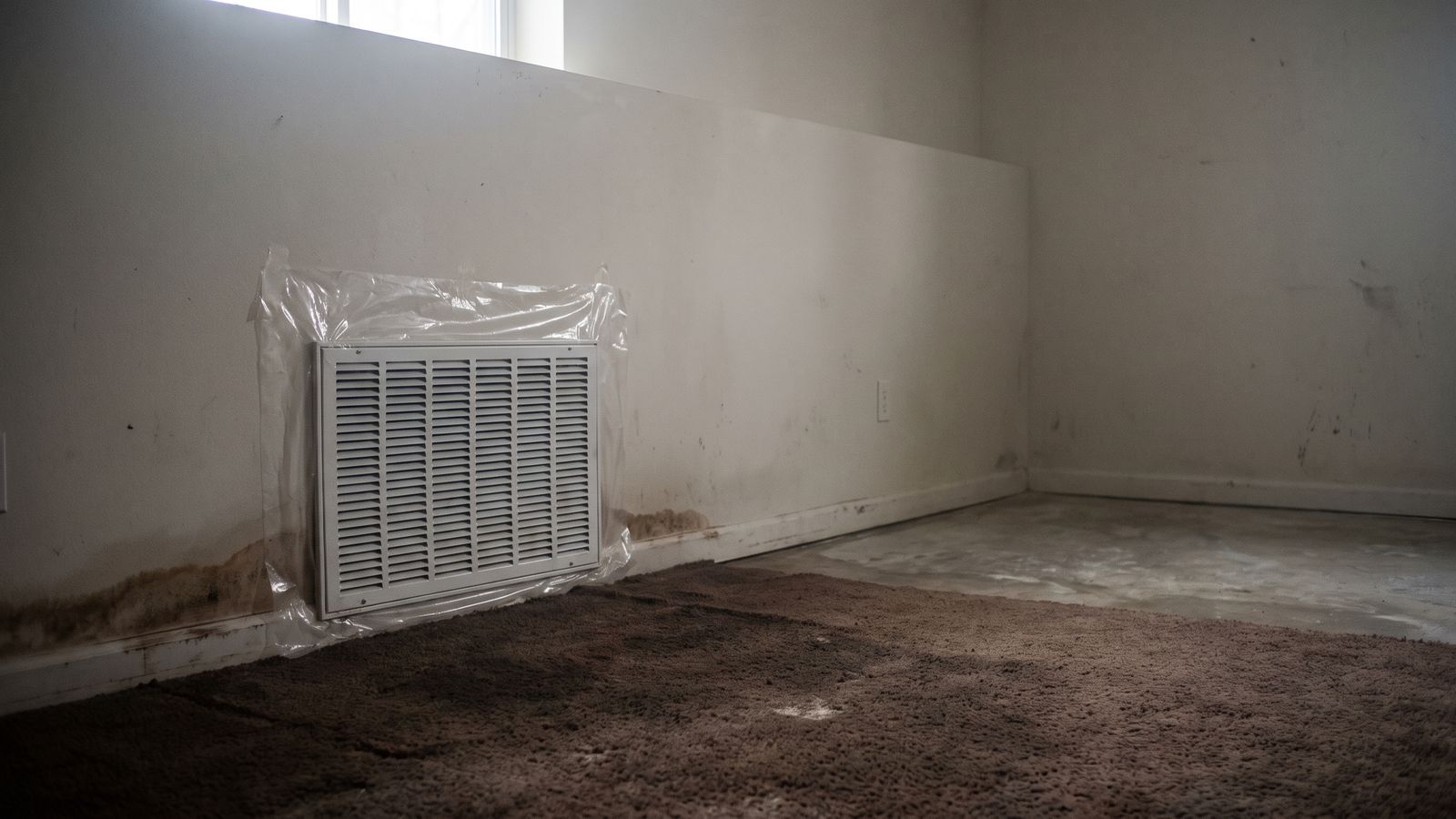 Return-air grille sealed off above a wet carpet Plastic sheeting taped over a basement return-air grille during sewage backup cleanup, wet carpet below