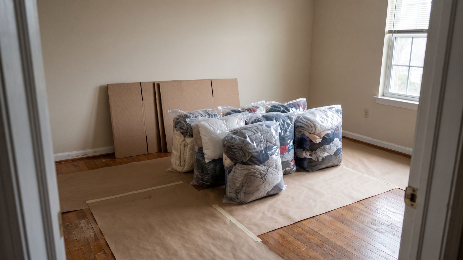 Sealed clear bags of bedding and clothing staged on kraft paper for a smoke damage pack-out, flat cartons behind.