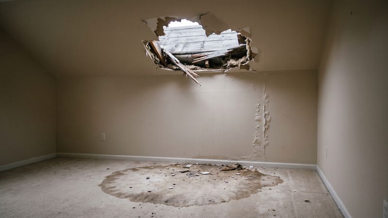 Storm breach torn through a bedroom ceiling above a wet carpet ring, before storm damage restoration