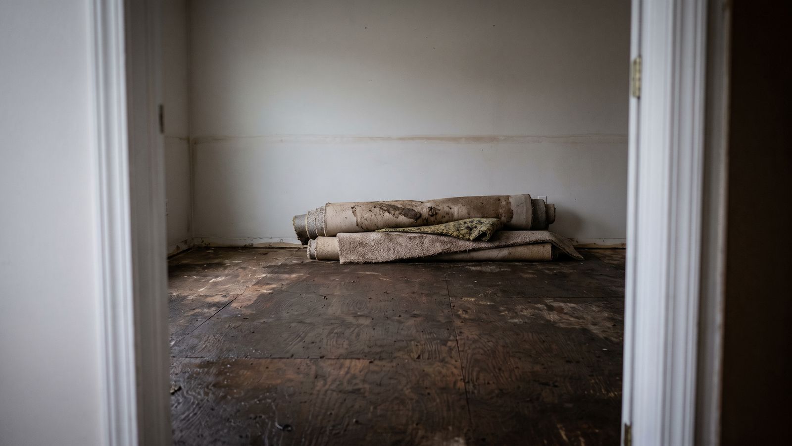 Bare plywood subfloor and rolled wet carpet in an emptied room during storm damage restoration