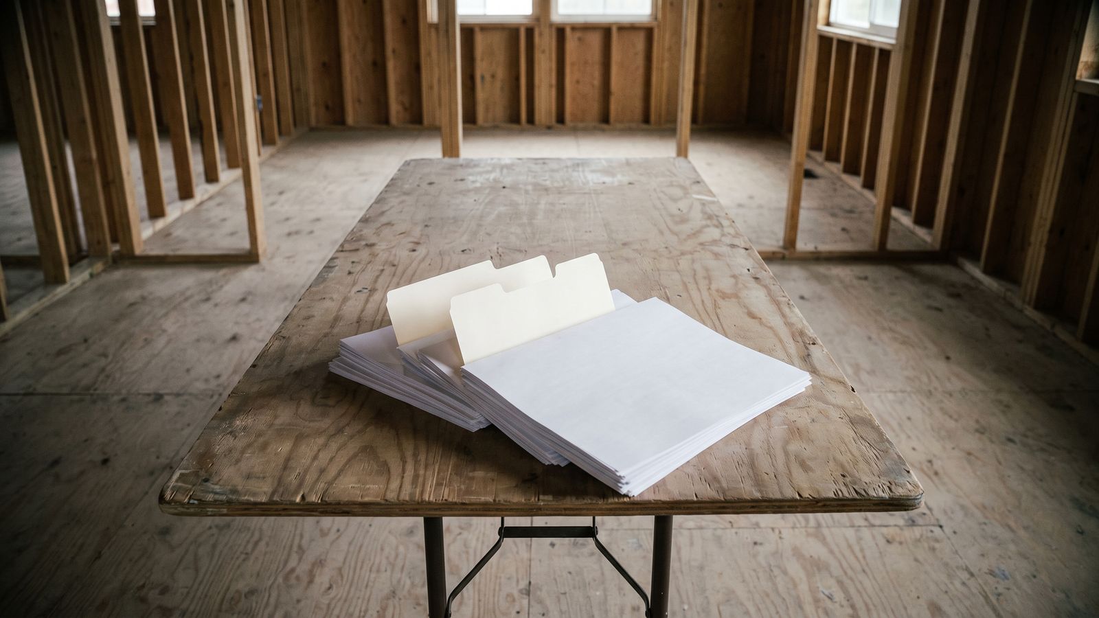 A claim file squared up before it is filed A squared stack of unmarked white sheets with manila tab dividers on a plywood folding table in a stripped wood-framed room.