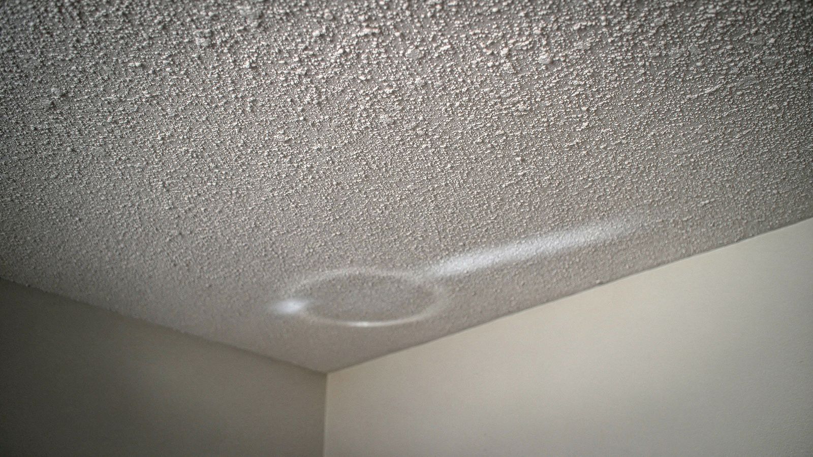 Popcorn ceiling texture and a faint water ring Popcorn ceiling texture close up in raking light, a faint water ring spreading near the wall line of an empty room