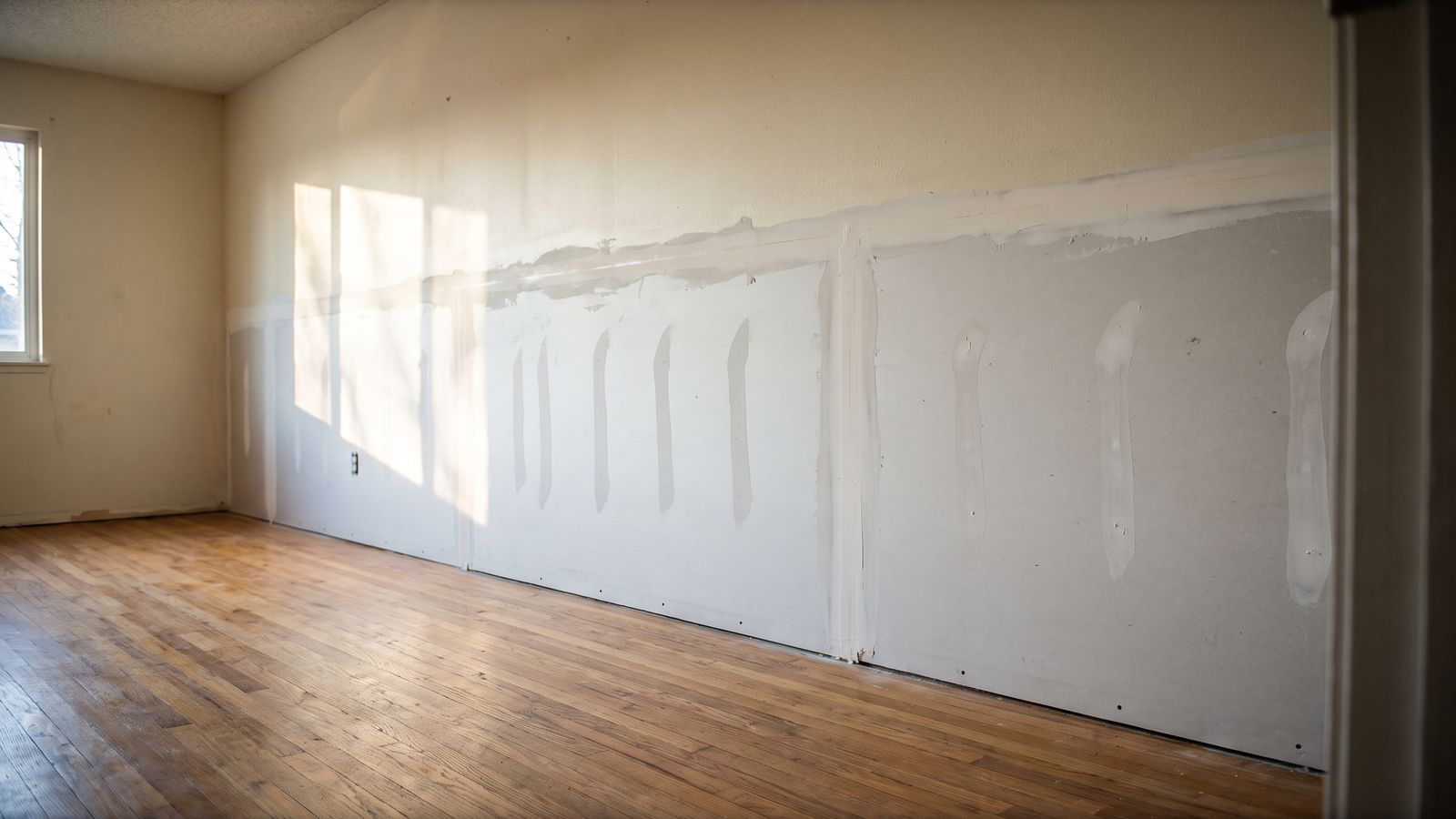 New lower drywall taped and feathered above an oak floor, the rebuild half of a water damage restoration cost