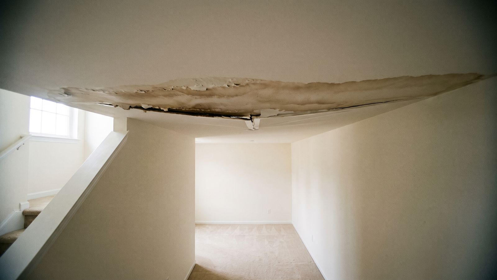 Stained and blistered hallway ceiling Brown tide line and blistered paint across a hallway ceiling, a hidden-moisture warning sign for water damage restoration