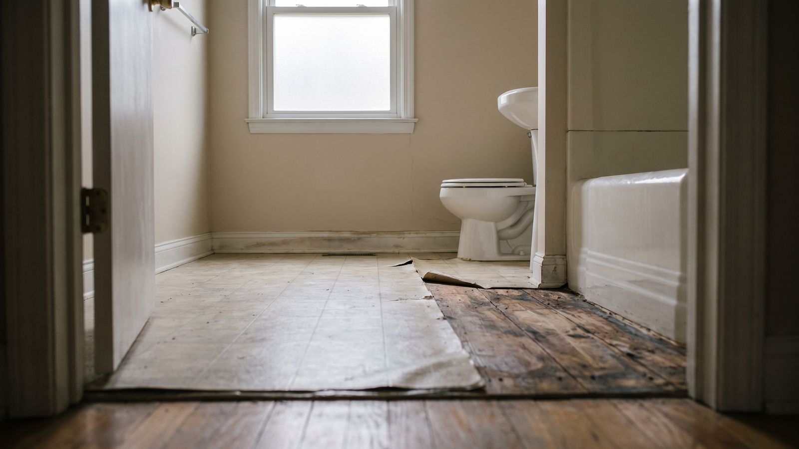 Lifted sheet vinyl exposing a water-stained bathroom subfloor that water damage restoration has to dry