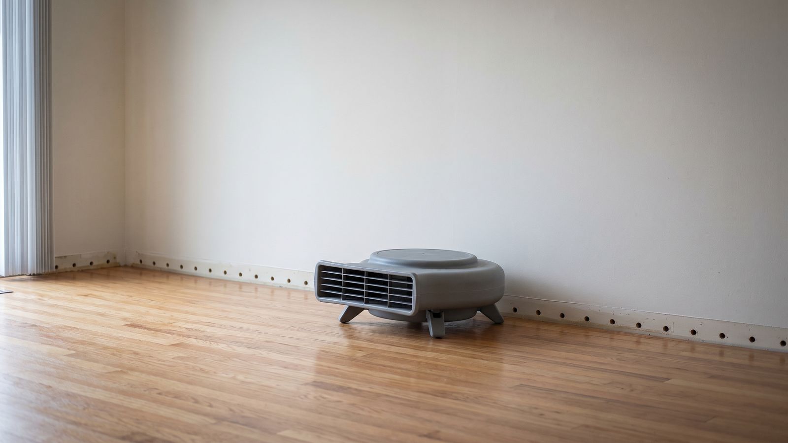 Centrifugal air mover beside a row of drilled weep holes at the base of water damaged drywall