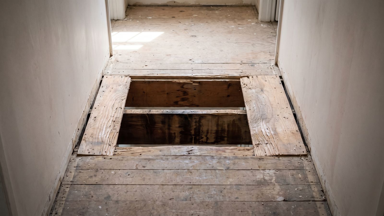 Rectangular cut opened in a hallway subfloor exposing dark stained framing, confirming water damaged subfloor signs