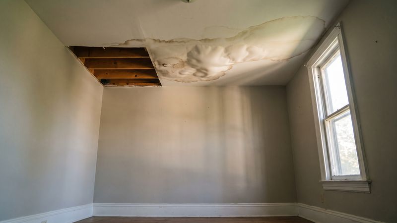 Sagging brown-stained ceiling cut open to bare joists in one corner of an empty room after water leak damage