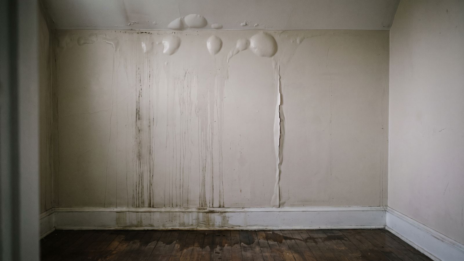 Water tracking down a wall below the ceiling line Water tracking down a painted wall from the ceiling line, paint blistered and floor dark with water leak damage