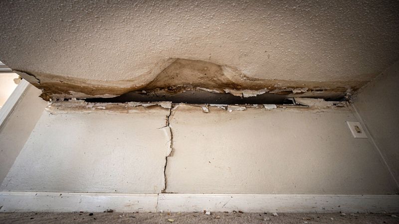 Brown-stained textured ceiling sagging and split open along the wall seam: water leak from upstairs neighbor ceiling