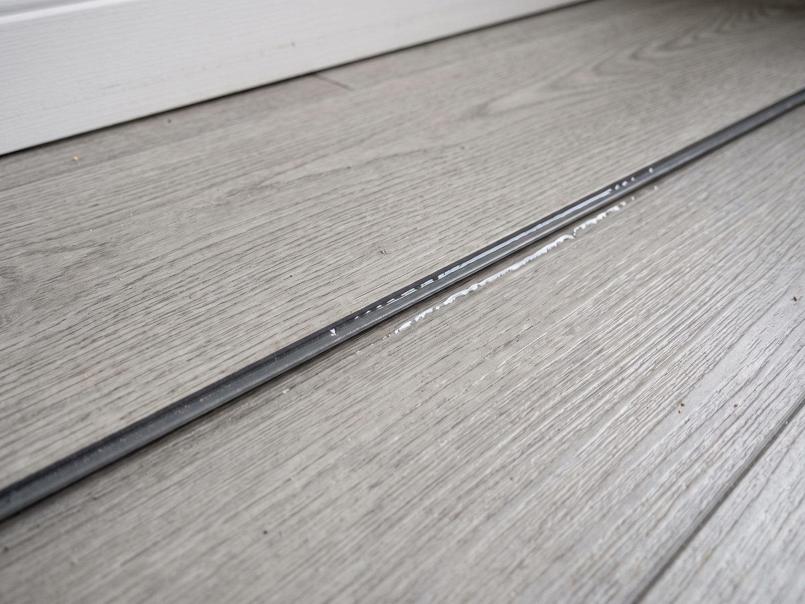 Water tracking along a vinyl plank seam Close view of the gap between two vinyl planks against a white baseboard, with water beading along the joint.
