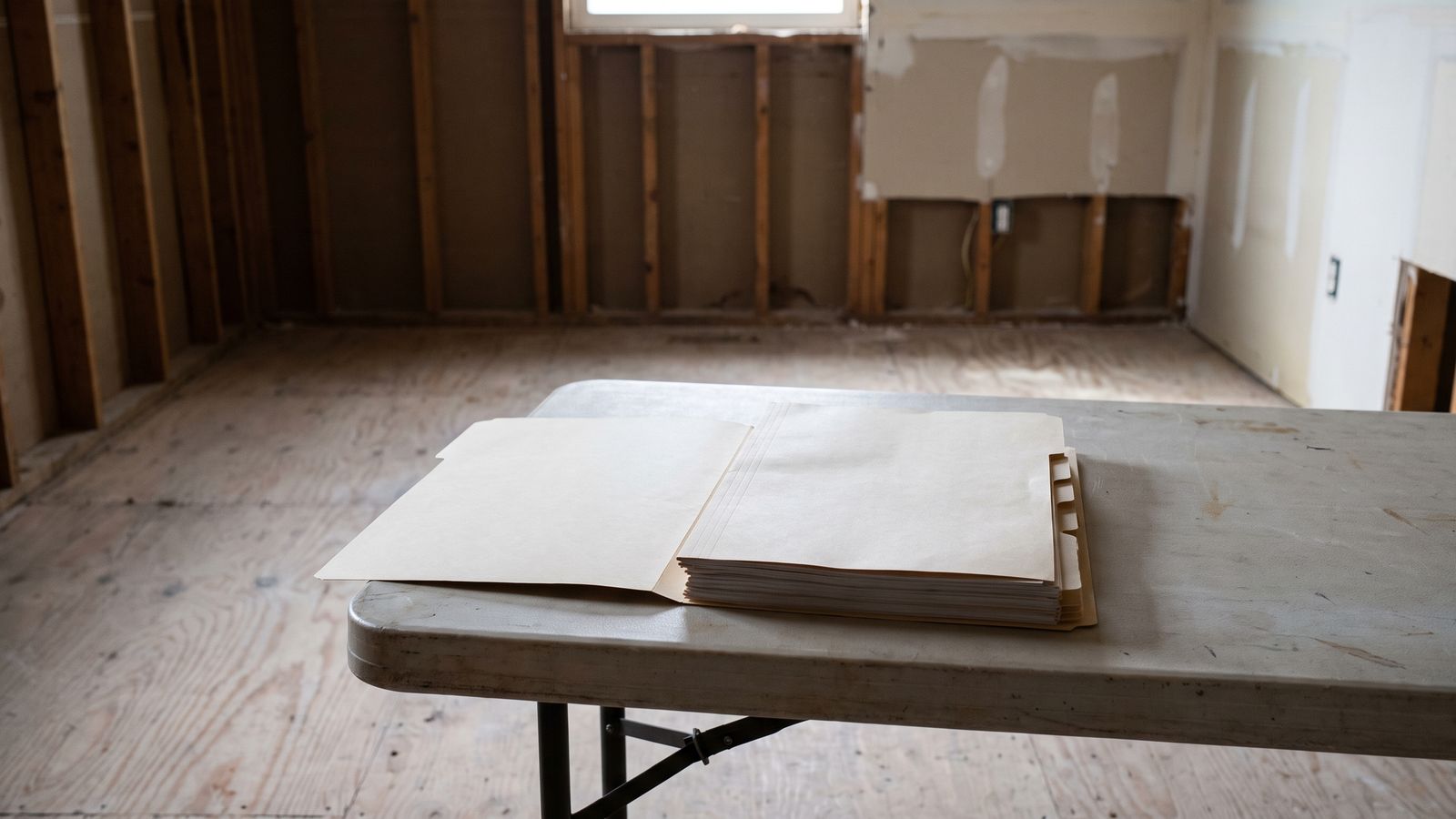 A tabbed documentation packet on a folding table A thick tabbed paper folder opened flat on a folding table in a stripped wood-framed room, tab dividers visible and blank.