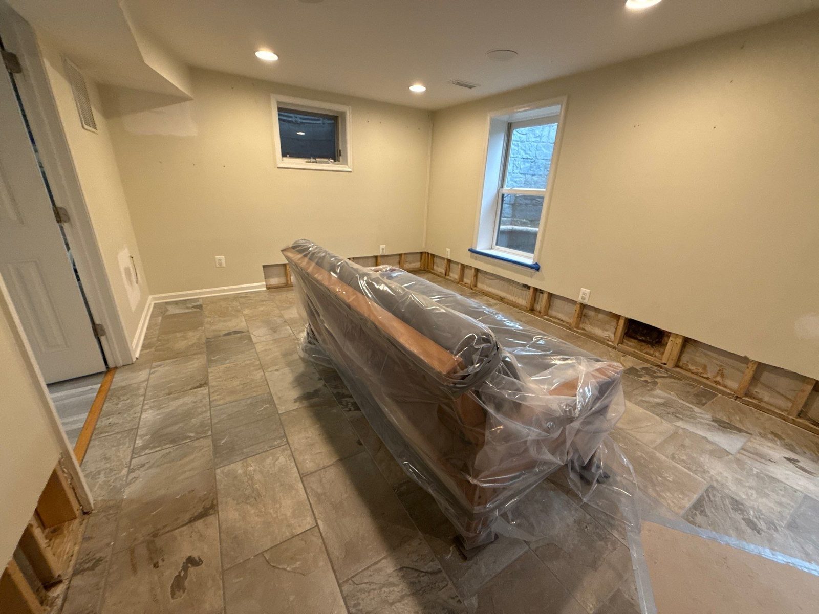 Basement in Annandale, VA with the lower wall cut open for drying and a sofa wrapped in plastic