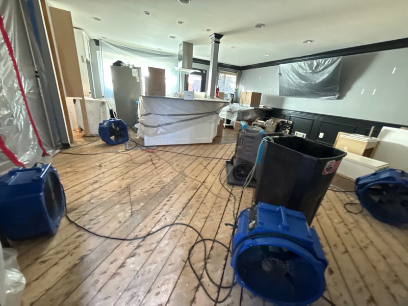 Air movers and dehumidifiers running across a water-damaged floor on a documented Restoration Doctor project