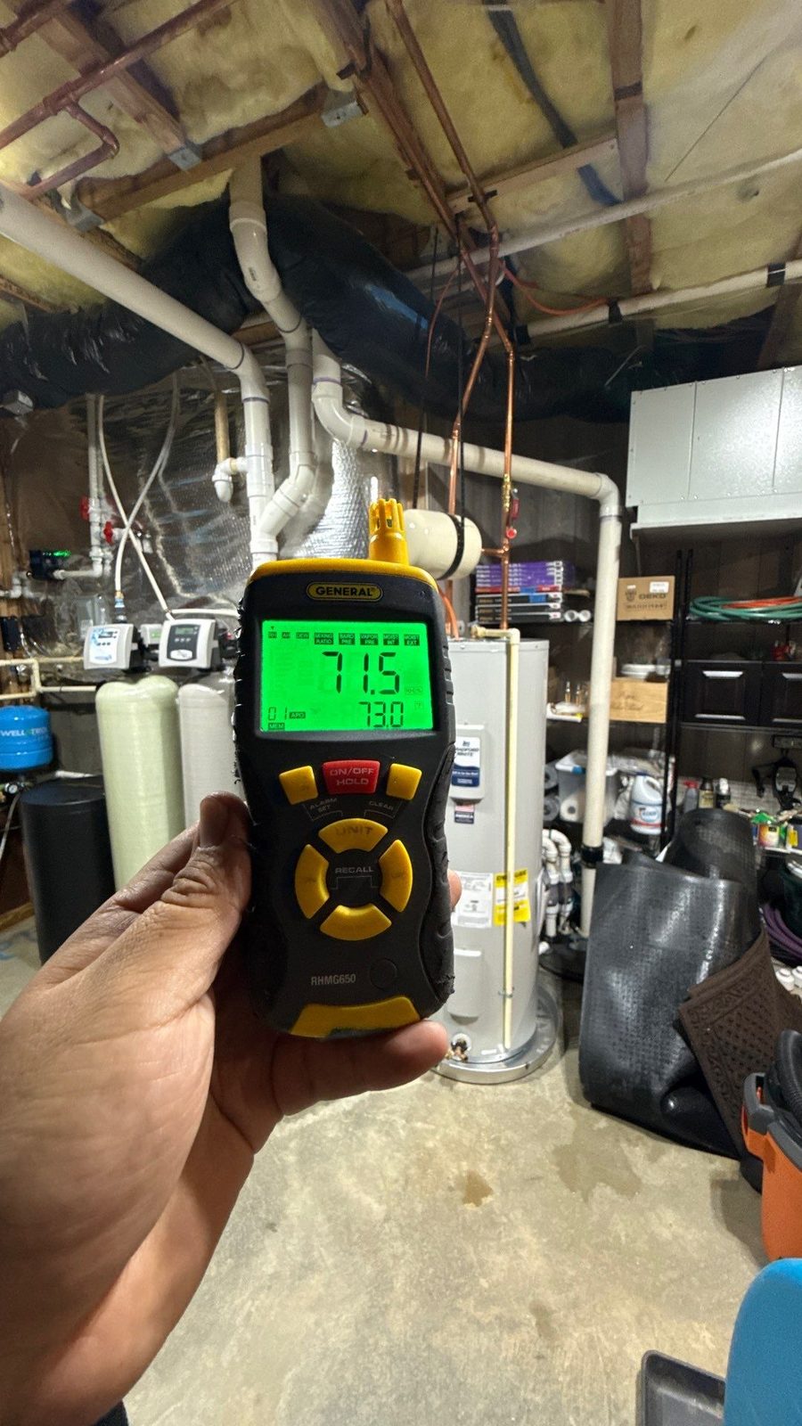 Handheld meter reading 71.5 percent relative humidity in a basement mechanical room with water heaters and pipes, McLean, VA, October 24, 2025