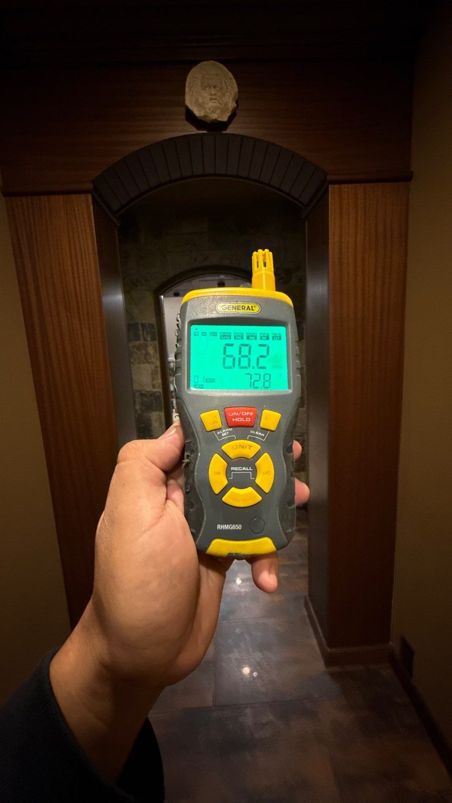Handheld meter reading 68.2 percent relative humidity in an arched wood doorway in a basement hallway, McLean, VA, October 24, 2025