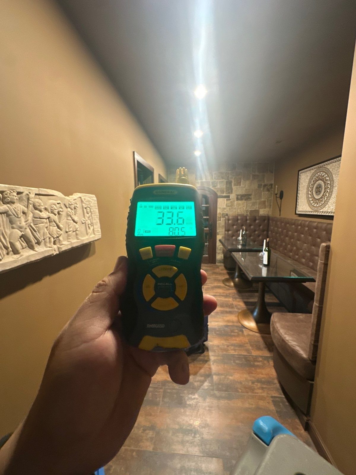 Handheld meter reading 33.6 percent relative humidity in a basement hallway with a stone accent wall, McLean, VA, October 26, 2025