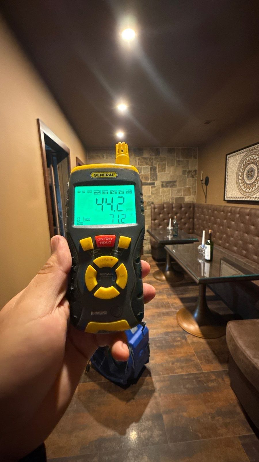 Handheld meter reading 44.2 percent relative humidity in a basement hallway with a stone accent wall, McLean, VA, October 28, 2025