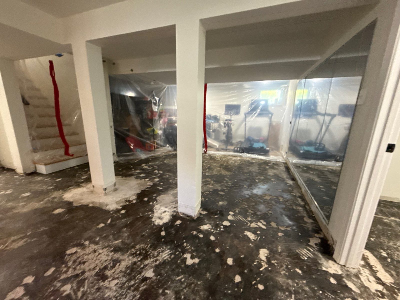 Basement with plastic barriers hung between support posts and a dark, stained floor with white patches, Arlington, VA, September 2026