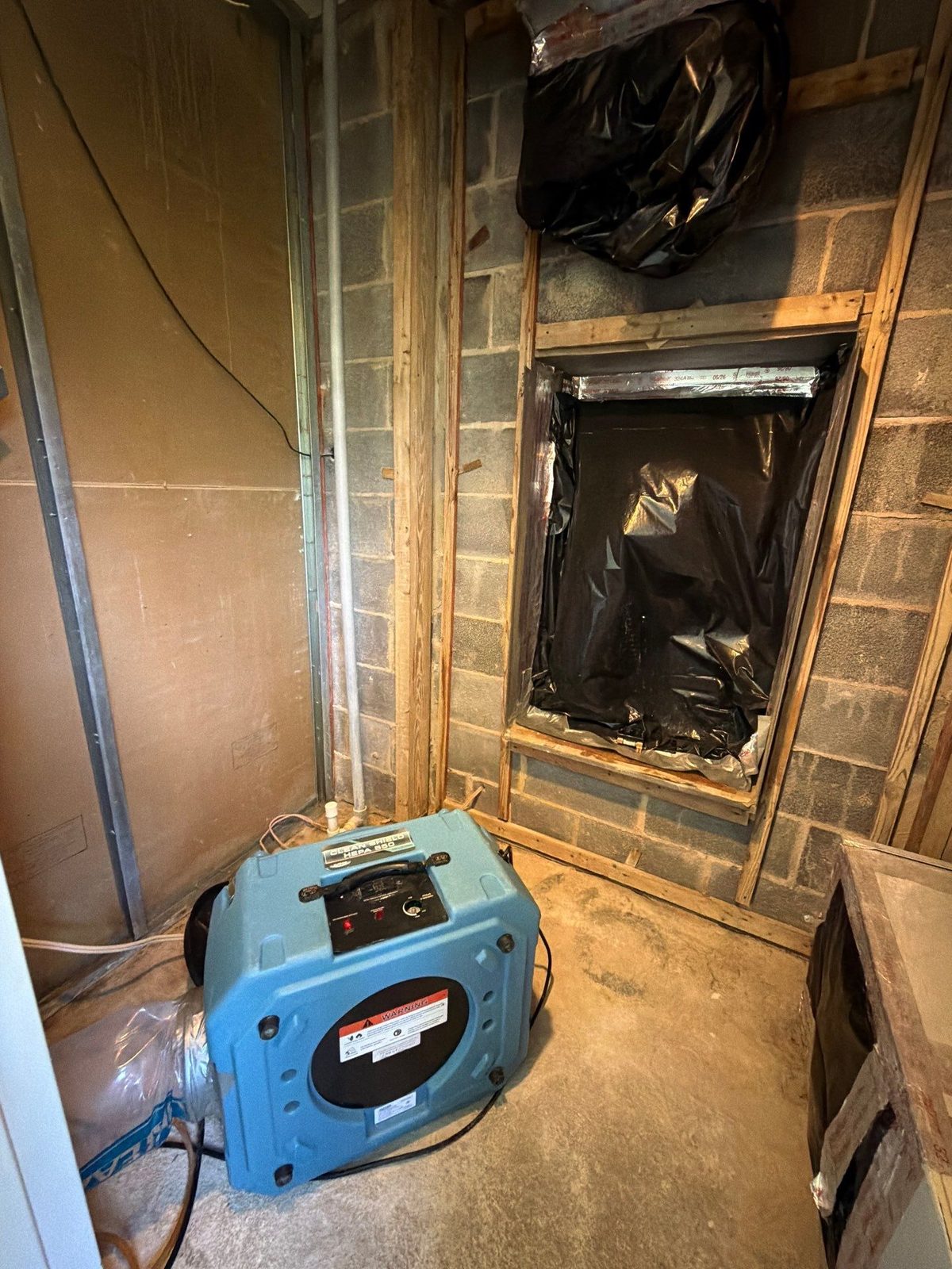 HEPA air filtration unit with ducting in a closet with a stripped concrete block wall, McLean, VA, September 2026