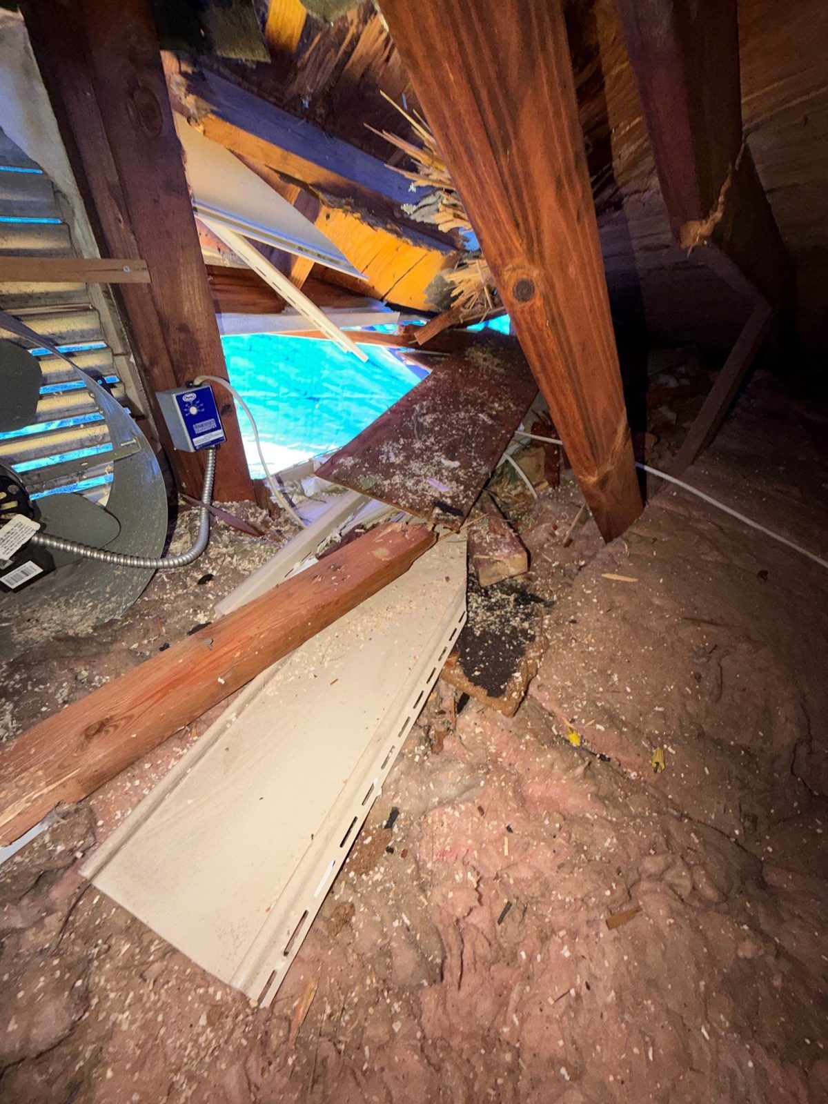 Broken roof framing and sheathing seen from inside an attic in Vienna, VA, with blue showing through the opening, March 2026