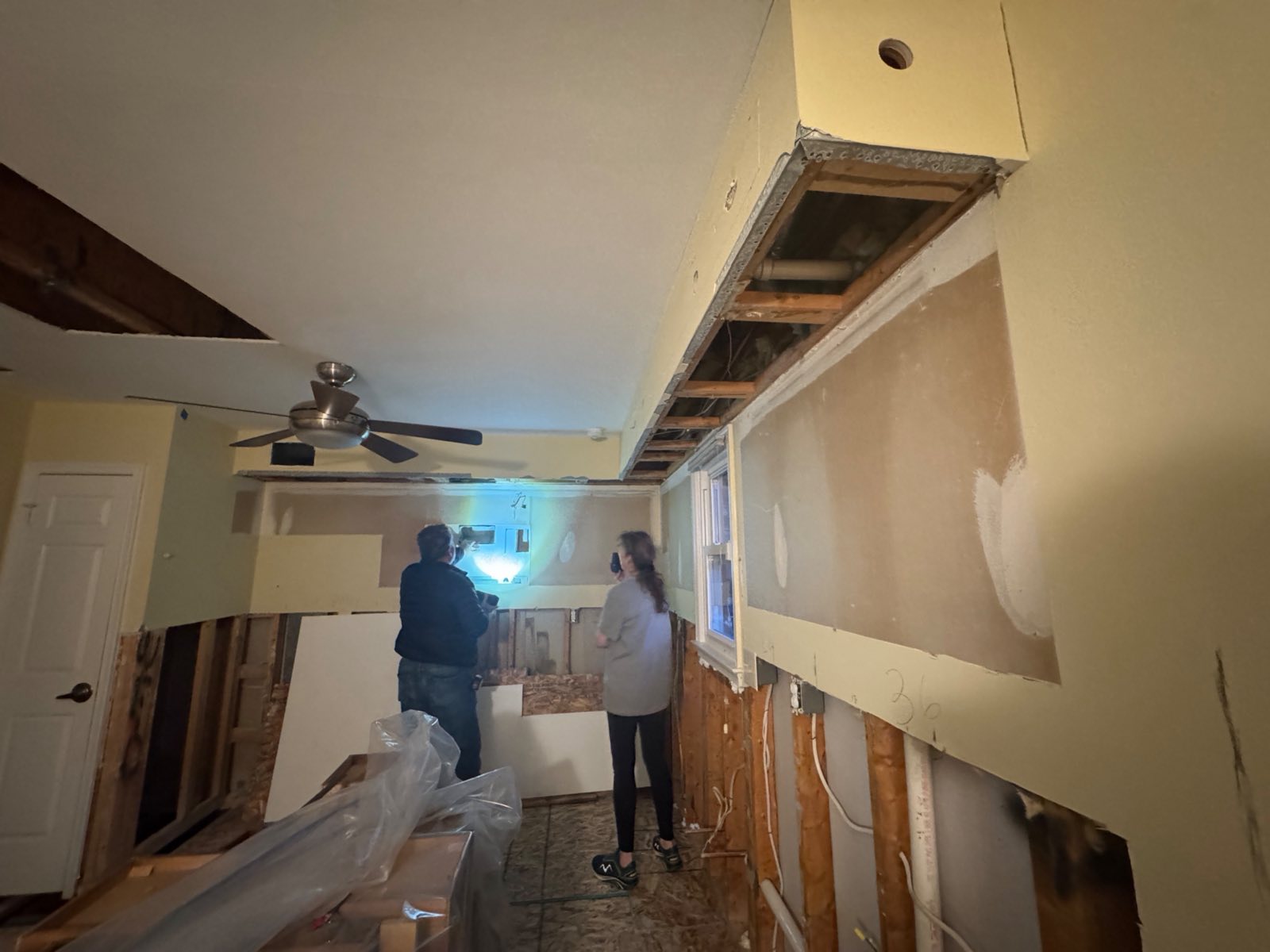 Two people inspecting opened kitchen walls and a ceiling cavity with a thermal imaging camera on a documented water damage project in Alexandria, VA