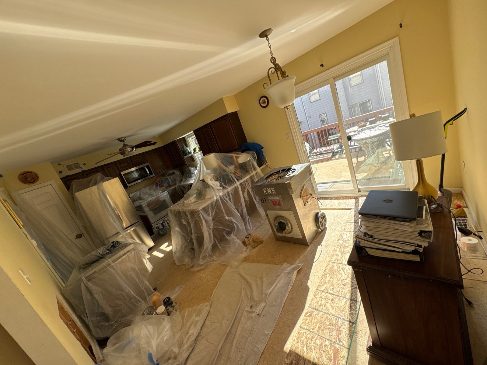 Kitchen and dining area in Alexandria, VA with appliances wrapped in plastic and a large drying machine running on the exposed subfloor