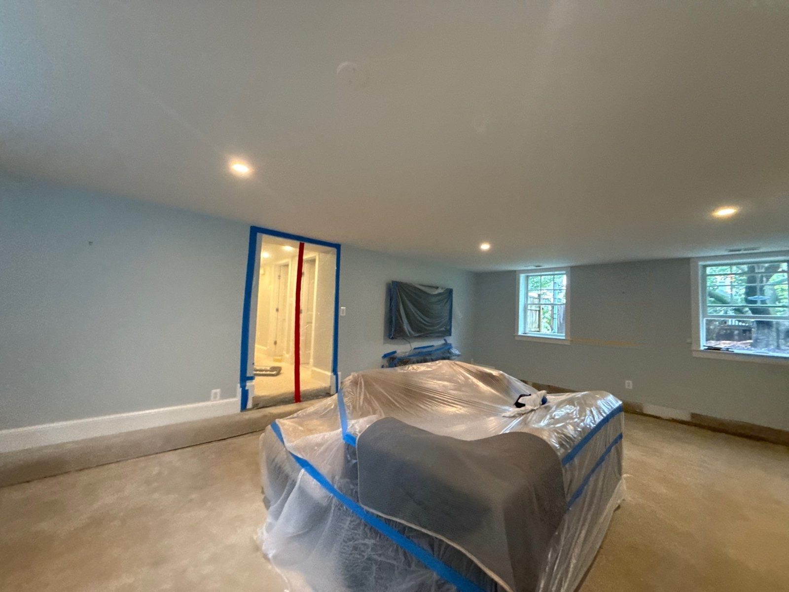 Arlington, VA basement with the furniture wrapped in plastic, the doorway sealed with tape and a zippered barrier, and the carpet removed